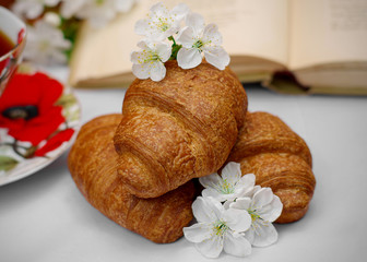 Croissants decorated with spring flowers. A cup of tea. Open book. Light background. Close-up. Spring.