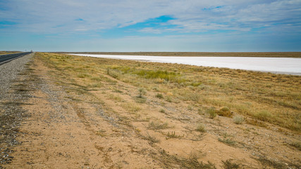 Highway in the hot endless steppe. The air temperature in the shade is 39 degrees Celsius. Along the road are salt marshes - a crust of salt on the ground.