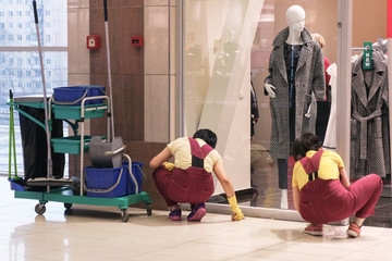 Image of the cleaners at the Mall. Two women wipe stains on the floor. Tools nearby.