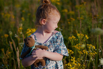 A little pretty girl in a blue summer dress picking flowers in the field of flowering yellow mustard on a sunny summer day. Kids and nature. Children in country. Beautiful flora.