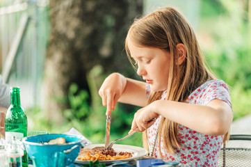 Little girl eating dinner on a terrace in outdoor restaurant