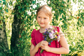 Summer portrait of cute little girl holding small bouquet of wild flowers - Powered by Adobe