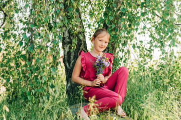 Summer portrait of cute little girl holding small bouquet of wild flowers