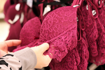 Woman chooses lace bra hanging on rack in lingerie store. Concept of shopping, customer during...