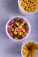 Multicolored pasta with the addition of natural vegetable dye. In a jar on a concrete table. Top view, copy Space.