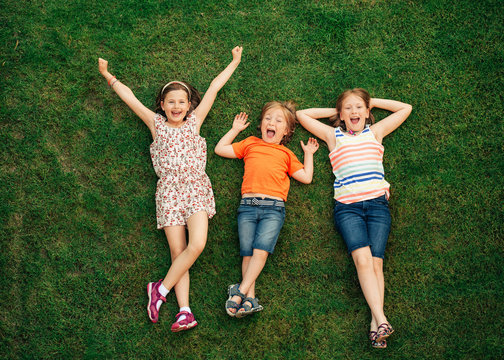 Happy children having fun outdoors. Kids playing in summer park. Little boy and two girls lying on green fresh grass