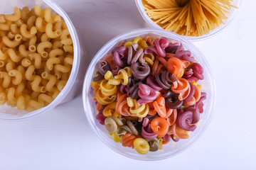 Multicolored pasta with the addition of natural vegetable dye. In a jar on a white table. Top view, copy Space.