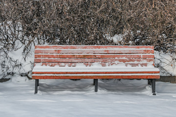 A wooden painted brown color beautiful bench with black wrought-iron legs stands with white snow in a park in winter