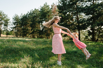 Portrait of a mother throws up and spins the daughter on hands on nature on summer day vacation. Mom and girl playing in the park at the sunset time. Concept of friendly family. Close Up.