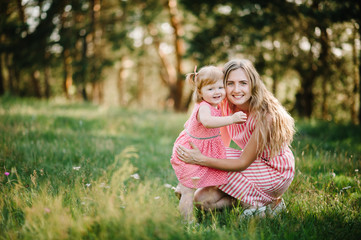 Fototapeta premium Portrait of a daughter hugging mother on nature on summer day vacation. Mom and girl playing in the park at the sunset time. Concept of friendly family. Close Up.