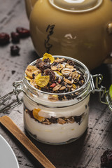 Glass full of white yogurt and muesli on dark wooden board