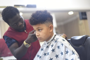 Boy in the african barbershop. Cute mixed boy makes a haircut in the African salon. Hair style. Haircut by machine for children. School boy hair style. 