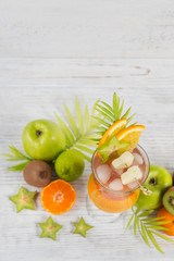 Summer cocktail with various tropical fruits around. Apple, kiwi, tangerine, orange, mango, carambola.