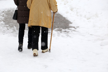 Woman walking with a cane during snowfall. Concept of limping, old age, winter weather, elderly or...