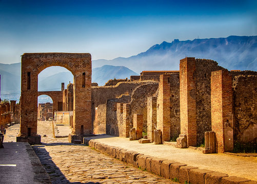 A stone gate and ruin of the city. Behind it is blue sky and big mountains