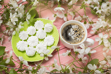 green plate with white meringues and a cup of coffee, on pink boards, surrounded by white flowers, spring concept