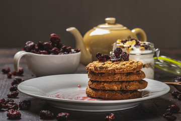 Several biscuits on white plate with dried berries on dark wooden board