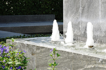 Fountain water spout spraying a pond, grass and flowers around.