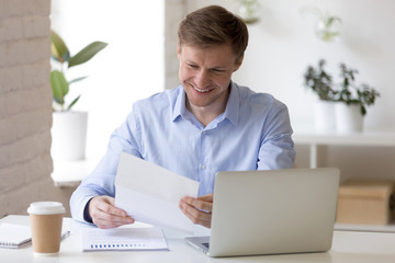 Satisfied businessman sitting at the desk reading letter 