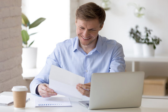 Satisfied businessman sitting at the desk reading letter 