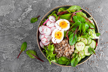 Buddha bowl dish with buckwheat porridge, boiled egg, fresh vegetable salad of radish, cucumber, lettuce and chard leaves. Healthy lunch menu. Top view
