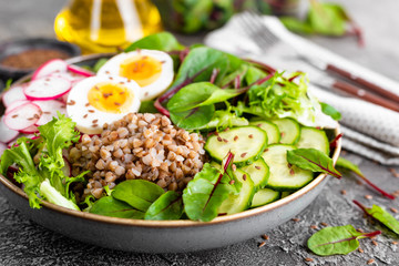 Buddha bowl dish with buckwheat porridge, boiled egg, fresh vegetable salad of radish, cucumber, lettuce and chard leaves. Healthy lunch menu