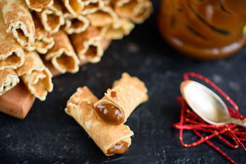 Fototapeta premium Wafer rolls, tasty and fragrant, with boiled condensed milk on a black table