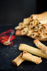 Wafer rolls, tasty and fragrant, with boiled condensed milk on a black table