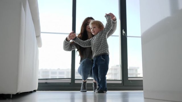 Fun and diversion young mother and little child son dancing near big window at home
