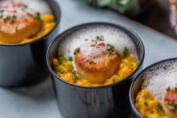 Orange pumpkin risotto with scallop and foamy sauce in black bowl on rustic wooden table