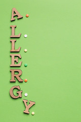 on the green background, the word allergy is laid out of letters, dandy multi-colored pills, the concept of allergy, copy space