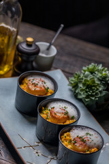 Orange pumpkin risotto with scallop and foamy sauce in black bowl on rustic wooden table