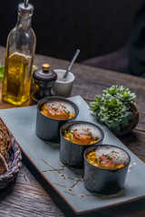 Orange pumpkin risotto with scallop and foamy sauce in black bowl on rustic wooden table