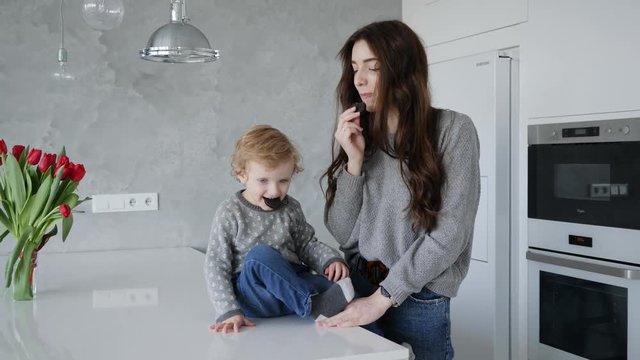 Beautiful family young mother with little boy son eating cookies together at home