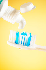 Toothpaste squeezed from tube onto brush on a yellow background, close up