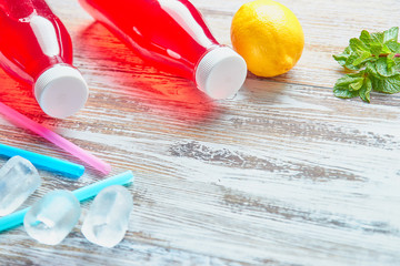 plastic bottles with berries, refreshing drink. scattered ice cubes and drinking straws. on the background of a shabby wooden table. close up. copy space.