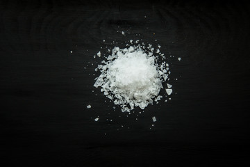 Close-up image of sea salt flakes on black wood background, view above