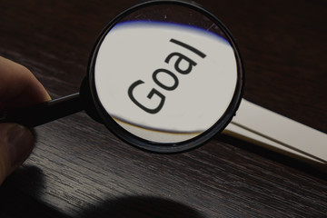 inscription GOAL on a white stick through a magnifying glass black background