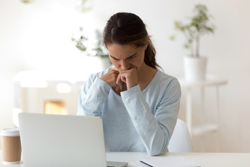 Gloomy young woman sitting at desk looking at computer screen