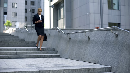 Businesswoman checking mail on smartphone, walking down stairs, workaholic