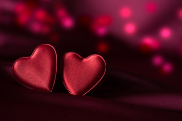 Two red hearts on purple satin with delicate red and purple bokeh in background