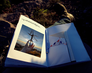 Open journal laying on jean clad leg, in the morning sun, with photo of Maine sunrise