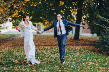 Lovers and smiling newlyweds stroll and have fun in the autumn in the park with yellow leaves. Portrait of a stylish groom with glasses and a cute bride in a white dress. Wedding photography.