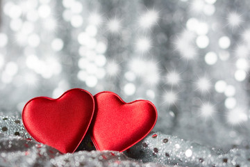 Fototapeta premium Two red hearts on silver fabric with sequins - silver background with stars and spots bokeh