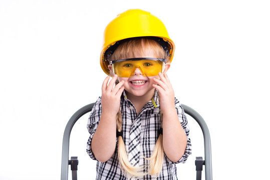 Little beautiful girl builder sits on the construction stairs in a yellow helmet