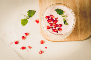 Yogurt. Yogurt with garnet and mint in glass on a wooden tray and the scattered pomegranate seeds on a white table. Top view. Sweet dessert