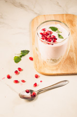 Yogurt. Yogurt with garnet and mint in glass on a wooden tray and the scattered pomegranate seeds on a white marble table. Sweet dessert