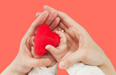 Heart in the hands of a child and mother, isolated on a living coral background. The concept of health and love