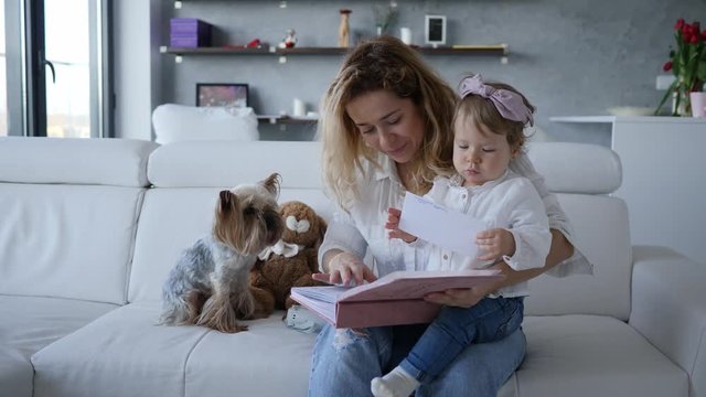 Mother with baby child daughter and pet dog watching family photo album at home