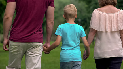 Family with kid holding hands, walking away, togetherness and family support - obrazy, fototapety, plakaty